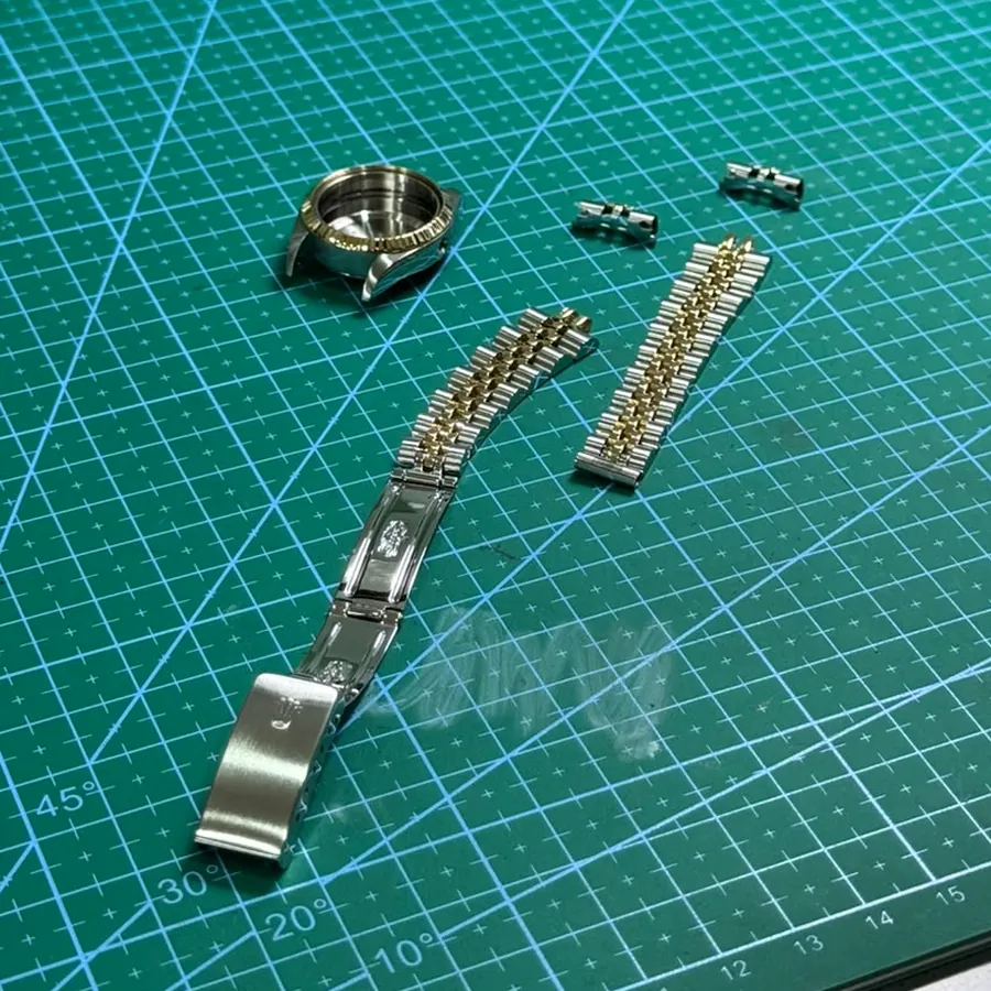 A watch case and bracelet stripped down on the bench mat